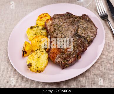 Auf dem runden weißen Teller liegt saftig gebratene Scheibe Kalbsfilet, garniert mit gedünsteten Kartoffeln Stockfoto