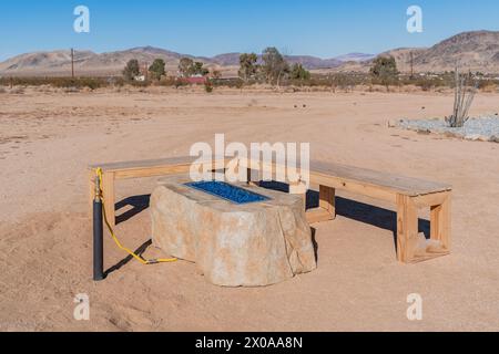 Fake Faux Rock Gas Kamin im Freien mit Holzbank in einem Wüstenhinterhof Stockfoto