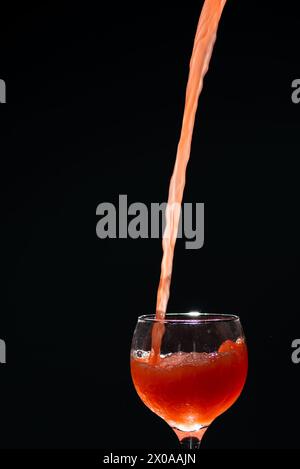 Guavasaft fällt in einen Glasbecher, der von einer Hand gehalten wird. Isoliert auf dunklem Hintergrund. Stockfoto