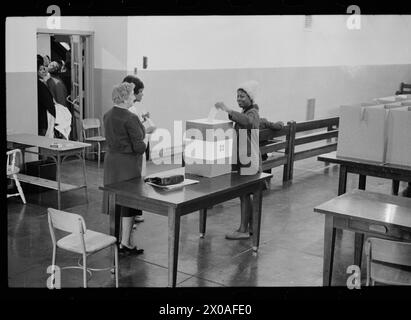 Das Foto zeigt eine junge Frau, die ihren Wahlzettel an der Cardozo High School abgibt, die von Wahlhelfern überwacht wird, während andere Wähler draußen in einem Flur warten, Washington, District of Columbia, 3. November 1964. Foto von Marion S Trikosko/US News and World Report Collection) Stockfoto