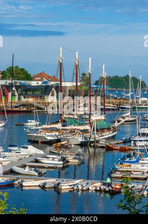 Eine lebhafte Szene mit großen Schiffen, Schlauchbooten und Segelbooten, die am Camden Harbor in Camden, Maine, USA, mit farbenfrohen Gebäuden und einem klaren blauen Himmel vor Anker liegen Stockfoto