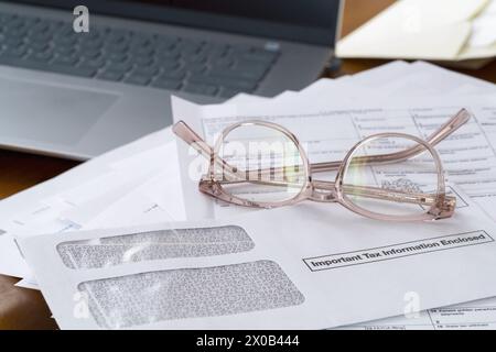 Chappaqua, NY - 9. April 2024: Laptop, Lesebrille mit Dokumenten, Einkommensteuerformulare und Umschlag oben mit wichtigen Steuerinformationen. Stockfoto