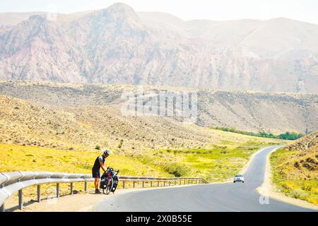 Man steht am Fahrradtouren in den Bergen am Straßenrand und hat Pause. Alleinreise mit Fahrradtaschen. Langzeitreisen in der Umgebung Stockfoto