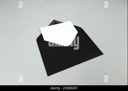Draufsicht des schwarzen Umschlags, weiße Karte auf grauem Hintergrund. Pfosten Sie flach. Kopierbereich. Stockfoto