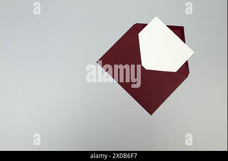 Draufsicht des roten Umschlags, weiße Karte auf grauem Hintergrund. Pfosten Sie flach. Kopierbereich. Stockfoto