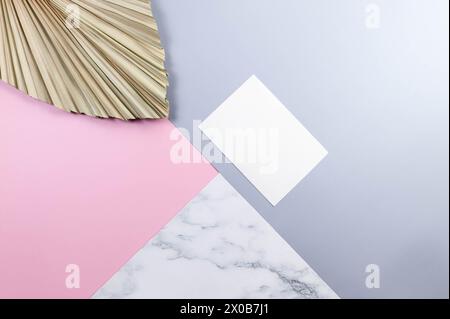 Draufsicht auf weiße Karte und getrocknete Palmblätter auf farbenfrohem Hintergrund. Blauer, rosafarbener und Marmorhintergrund. Pastellfarbene Tapete mit Marmorstruktur. Stockfoto