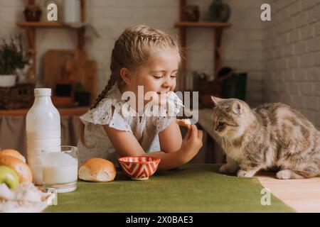 Ein süßes Mädchen in der Küche füttert eine Katze am Tisch. Hochwertige Fotos Stockfoto