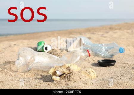 Wort SOS und Müll verstreut am Strand in der Nähe des Meeres. Recycling-Problem Stockfoto