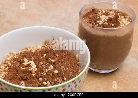 Eine Nahaufnahme eines Glases und einer Schüssel, gefüllt mit einem Schokoladenmousse, angereichert mit Kakao und Mandeln auf einer Arbeitsplatte. Schnelle und einfache Desserts. Stockfoto