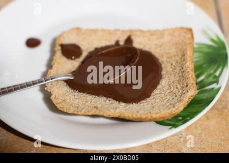 Ein Nahaufnahme-Bild, das den wunderbaren Moment des Verbreitens von reichhaltiger, cremiger Schokolade auf einer frischen Brotscheibe auf einem lebendigen Teller feststellt. H Stockfoto