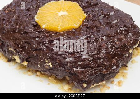 Nahaufnahme eines eleganten Schokoladendesserts, verziert mit einer frischen Orangenscheibe, präsentiert auf einem unberührten weißen Teller mit Haselnussbasis. Stockfoto