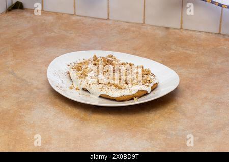 Ein hausgemachtes Karottenkuchen-Dessert mit einer cremigen Basis, garniert mit einer knusprigen Garnitur aus Walnüssen und Zimt auf einem klassischen weißen Teller vor dem Hintergrund Stockfoto