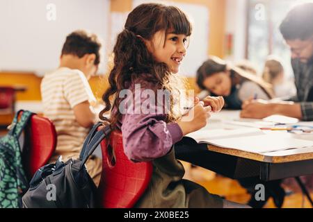 Bildung und Kinderentwicklung. Das kleine Mädchen lächelt, während es in einer Klasse mit ihrem Lehrer und Mitschülern sitzt. Eine Studentin nimmt sich einen Moment in die Schule Stockfoto