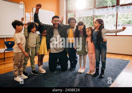 Eine Gruppe junger Schüler steht mit ihrem Lehrer in einem Klassenzimmer und feiert ihren Schulerfolg. Der Lehrer freut sich, die Kinder zu sehen Stockfoto