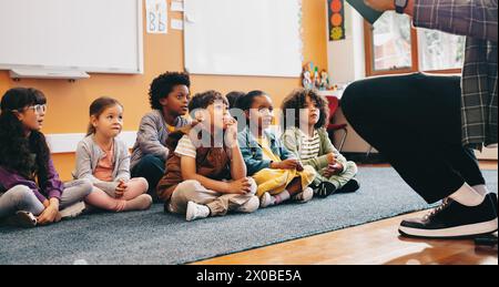 Grundschüler sitzen und hören sich eine Geschichte von ihrem Lehrer an. Gruppe von Kleinkindern mit Hörverständnis im Unterricht. Kind Stockfoto