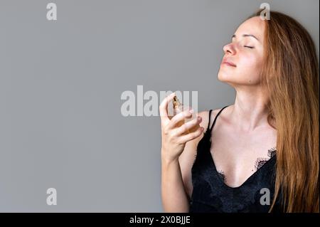 Die Frau sprüht ihr Parfüm auf den Hals und genießt den Duft von Parfüm. Stockfoto