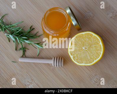 Glas frischer Rosmarinhonig mit frischer Zitrone auf einem hellen Holztisch, Stockfoto
