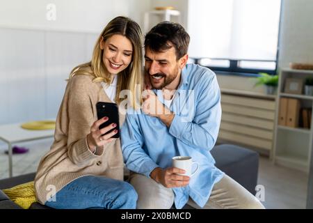 Ein junges glückliches Paar, das zu Hause Nachrichten aus sozialen Medien per Telefon mitteilt und online einkauft. Stockfoto