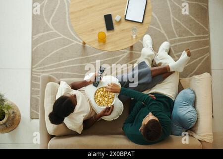 Ein Paar sitzt auf einem bequemen Sofa, isst Popcorn und sieht sich eine neue tv-Show an Stockfoto