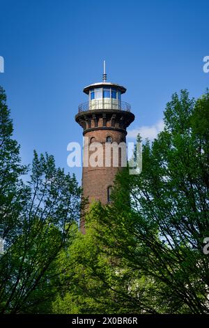 Der historische Leuchtturm helios hinter Bäumen und vor blauem Himmel Stockfoto