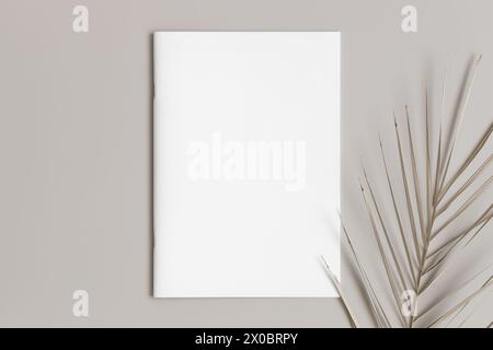 Zeitschriftenmockup mit einem Palmblatt auf dem beigefarbenen Tisch. Stockfoto