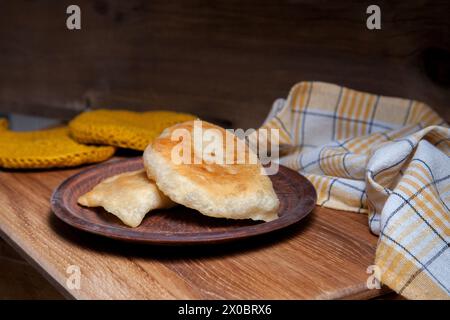 Tonplatte mit zwei einzelnen gebratenen Pasteten mit Fleisch auf Holztisch. Tatarische traditionelle Pasteten. Stockfoto