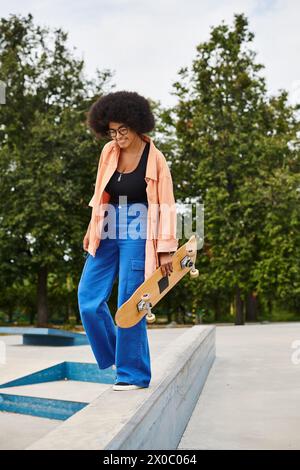 Eine junge Afroamerikanerin mit lockigen Haaren steht selbstbewusst mit ihrem Skateboard in einem Skatepark auf einem Felsvorsprung. Stockfoto