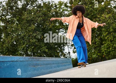 Eine junge Afroamerikanerin mit lockigen Haaren, die geschickt auf einem Skateboard die Seite einer Rampe in einem lebhaften Skatepark hinunterfährt. Stockfoto