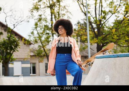 Die junge afroamerikanische Frau mit lockigen Haaren steht neben dem Skateboard auf einer Skateboard-Rampe in einem lebhaften Outdoor-Skatepark. Stockfoto