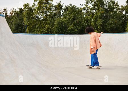 Eine junge Afroamerikanerin mit lockigen Haaren, die in einem Skatepark Skateboarden und Tricks auf den Rampen und Rails macht. Stockfoto