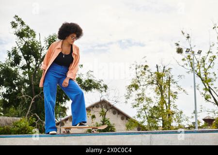 Junge afroamerikanische Frau mit lockigen Haaren, die Skateboard auf der Zementwand im Skatepark im Freien reitet. Stockfoto