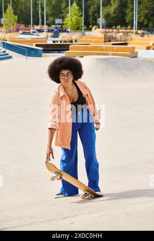 Die junge afroamerikanische Frau steht selbstbewusst auf einem Skateboard in einem belebten Skatepark und zeigt ihre Fähigkeiten und ihren Stil. Stockfoto