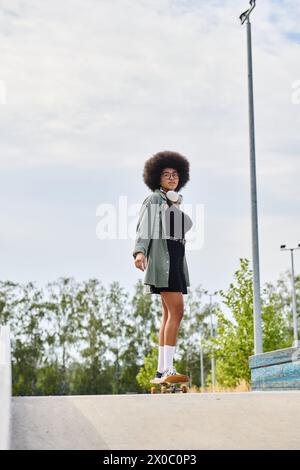 Eine junge afroamerikanische Frau mit lockigen Haaren balanciert geschickt auf einem Skateboard oben auf einer Rampe in einem lebhaften Skatepark. Stockfoto