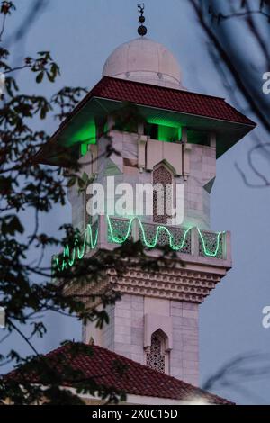 Eine majestätische weiße Moschee mit einem hoch aufragenden, beleuchteten Minarett durchdringt den Nachthimmel, seine Fenster leuchten mit warmem Licht. Nach Dem Ramadan. Grüne Farbe Stockfoto