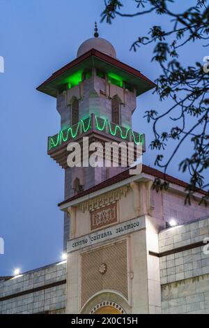 Eine majestätische weiße Moschee mit einem hoch aufragenden, beleuchteten Minarett durchdringt den Nachthimmel, seine Fenster leuchten mit warmem Licht. Nach Dem Ramadan. Grüne Farbe Stockfoto