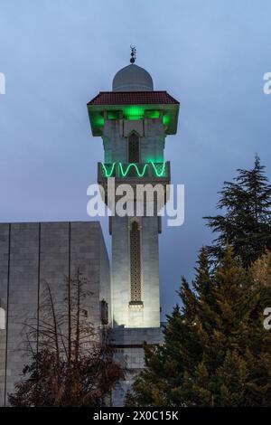 Eine majestätische weiße Moschee mit einem hoch aufragenden, beleuchteten Minarett durchdringt den Nachthimmel, seine Fenster leuchten mit warmem Licht. Nach Dem Ramadan. Grüne Farbe Stockfoto