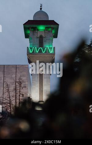 Eine majestätische weiße Moschee mit einem hoch aufragenden, beleuchteten Minarett durchdringt den Nachthimmel, seine Fenster leuchten mit warmem Licht. Nach Dem Ramadan. Grüne Farbe Stockfoto