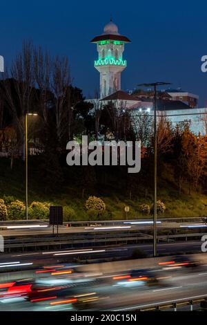 Eine majestätische weiße Moschee mit einem hoch aufragenden, beleuchteten Minarett durchdringt den Nachthimmel, seine Fenster leuchten mit warmem Licht. Nach Dem Ramadan. Grüne Farbe Stockfoto