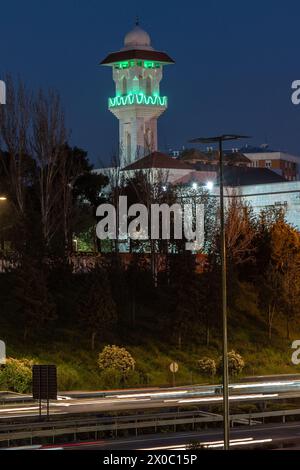 Eine majestätische weiße Moschee mit einem hoch aufragenden, beleuchteten Minarett durchdringt den Nachthimmel, seine Fenster leuchten mit warmem Licht. Nach Dem Ramadan. Grüne Farbe Stockfoto