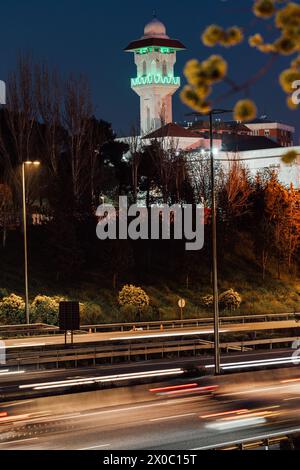 Eine majestätische weiße Moschee mit einem hoch aufragenden, beleuchteten Minarett durchdringt den Nachthimmel, seine Fenster leuchten mit warmem Licht. Nach Dem Ramadan. Grüne Farbe Stockfoto