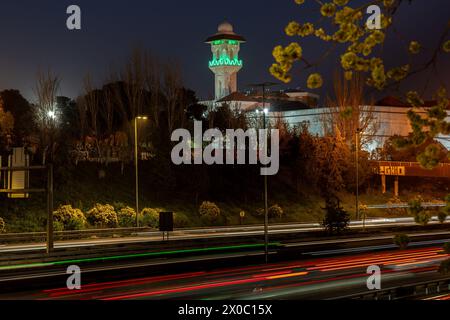 Eine majestätische weiße Moschee mit einem hoch aufragenden, beleuchteten Minarett durchdringt den Nachthimmel, seine Fenster leuchten mit warmem Licht. Nach Dem Ramadan. Grüne Farbe Stockfoto