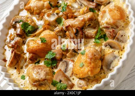 Hähnchenschenkel in cremiger Knoblauchsauce mit Kräutern und Parmesankäse in weißer Auflaufform, holländischer Blickwinkel, Nahaufnahme Stockfoto