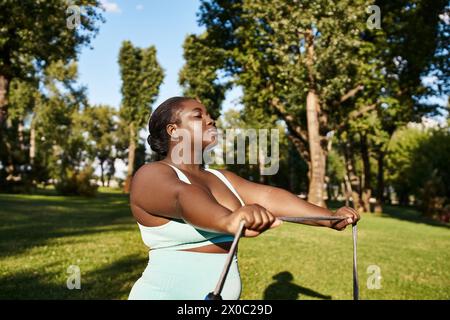 Eine Afroamerikanerin in Sportbekleidung hält selbstbewusst ein Seilspringen, bereit für eine Schaukel in einer malerischen Parklandschaft. Stockfoto