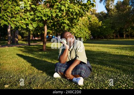 Eine besonders große afroamerikanische Frau sitzt im üppigen Gras, in der warmen Sommersonne voller Musik. Stockfoto