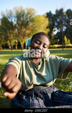 Die Frau entspannt sich im Gras, eingetaucht in Musik, die an einem sonnigen Tag über Kopfhörer spielt. Stockfoto