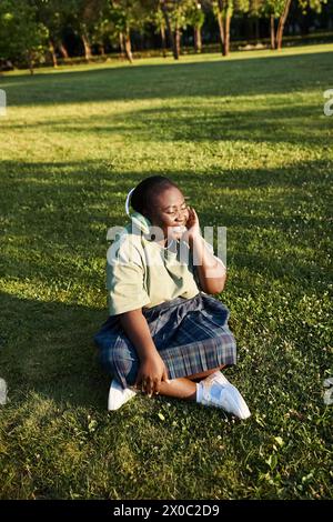 Die Frau entspannt sich im Gras, taucht in Musik ein, die über Kopfhörer spielt Stockfoto