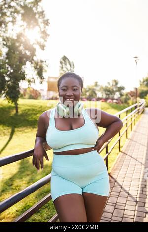 Eine Afroamerikanerin mit Kopfhörern, trägt ein blaues Oberteil und Shorts und posiert selbstbewusst für ein Foto im Freien. Stockfoto