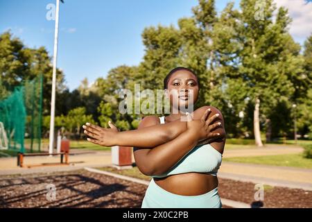 Kurvige Afroamerikanerin in Sportbekleidung, die anmutig in einem Park steht und ihre Arme draußen ausstreckt. Stockfoto