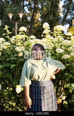 Eine Afroamerikanerin in Übergröße steht selbstbewusst vor einem Busch mit weißen Blumen und umrahmt die Schönheit der Natur um sie herum. Stockfoto