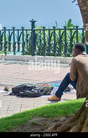 Tarragona, Spanien - 11. April 2024: In Tarragona reflektiert ein illegaler Verkäufer neben seinen Waren und bietet einen visuellen und emotionalen Kontrapunkt. Stockfoto